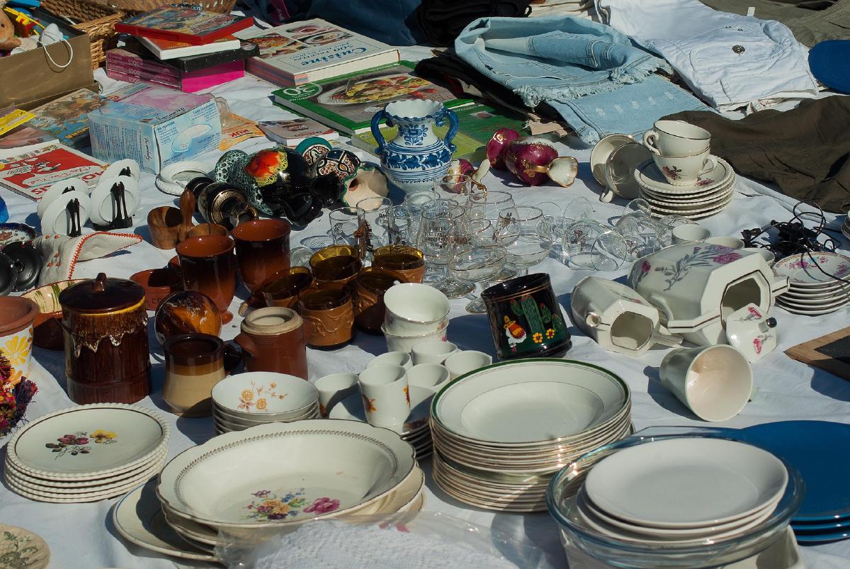 A table of dishes, glassware, mugs, and books laid out for a downsizing sale